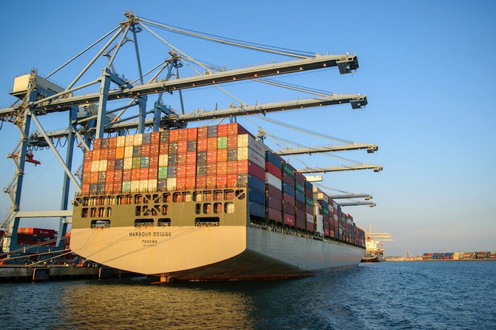 pexels-photo-24246926 A large container ship at an industrial harbor with cranes under a clear blue sky.