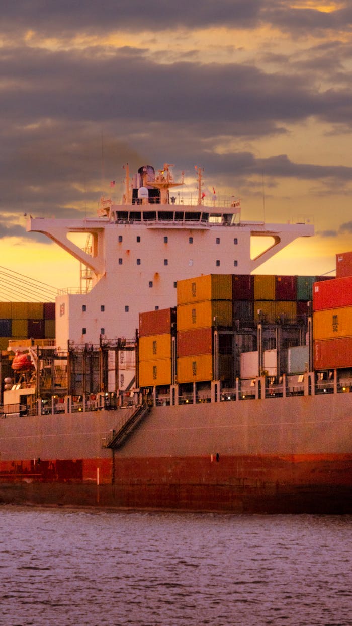 services-02 Cargo ship loaded with colorful containers against a vibrant sunset sky.
