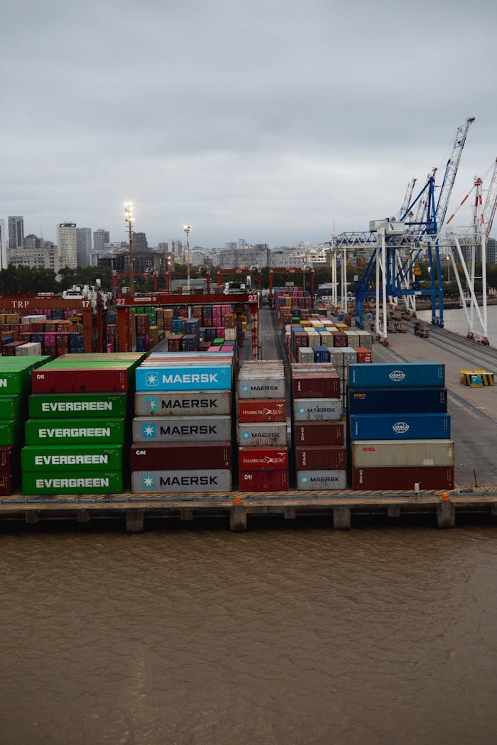 A bustling container port showcasing stacked shipping containers and cranes during a cloudy day.