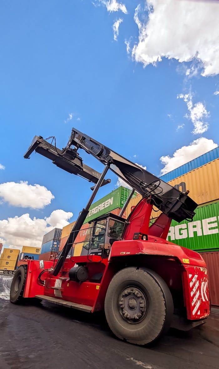 services-01 A vibrant red container handler operating at an industrial shipping port under a bright sky.